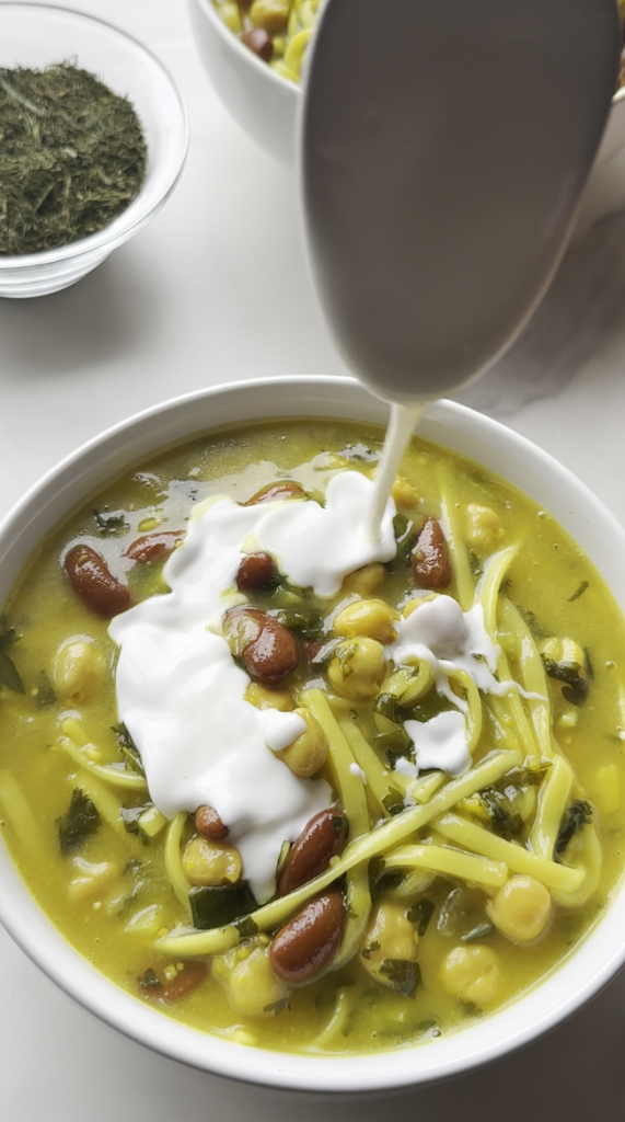 a bowl of aush/ash reshteh with yogurt being drizzled over